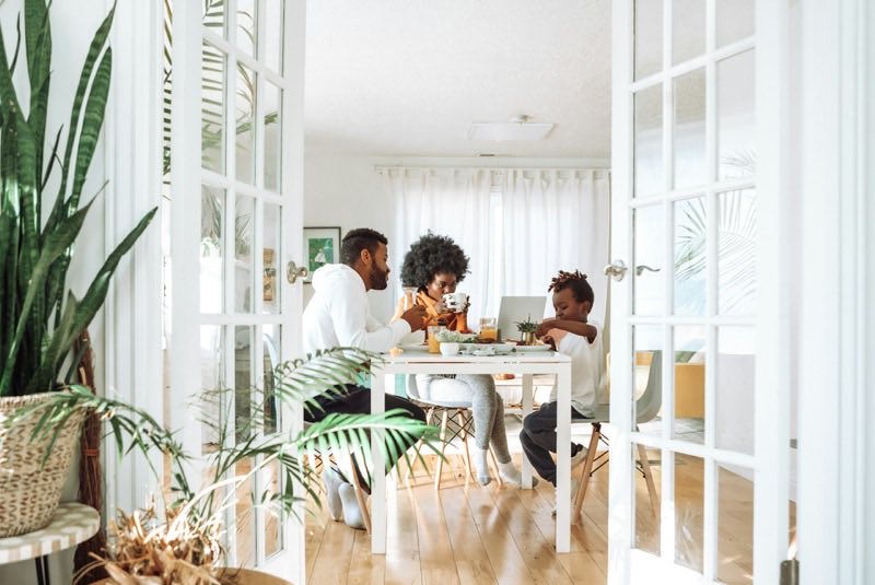 A family of three eating together at a dining table, seen through open French doors