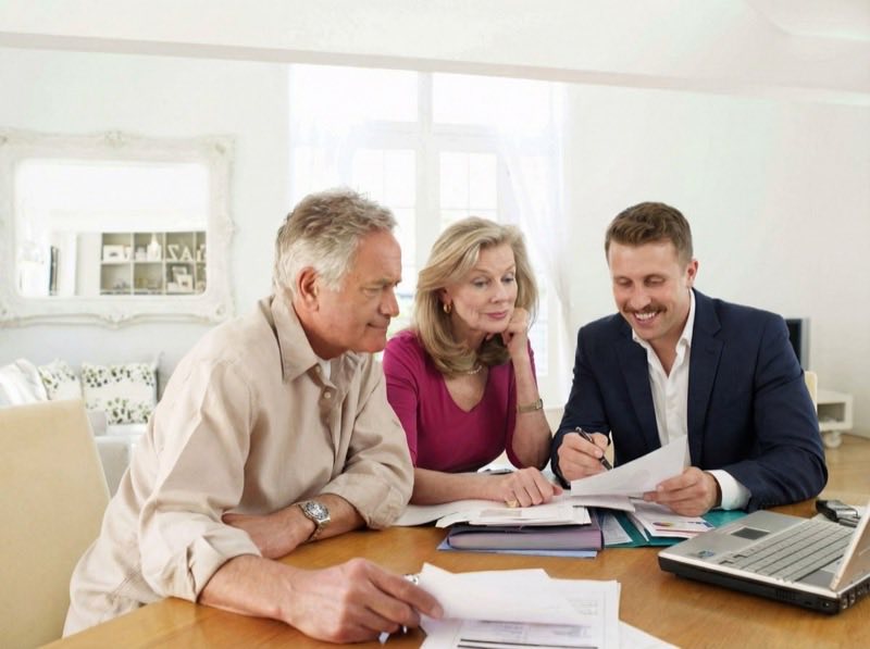An older couple reviewing documents at a dining table with an advisor