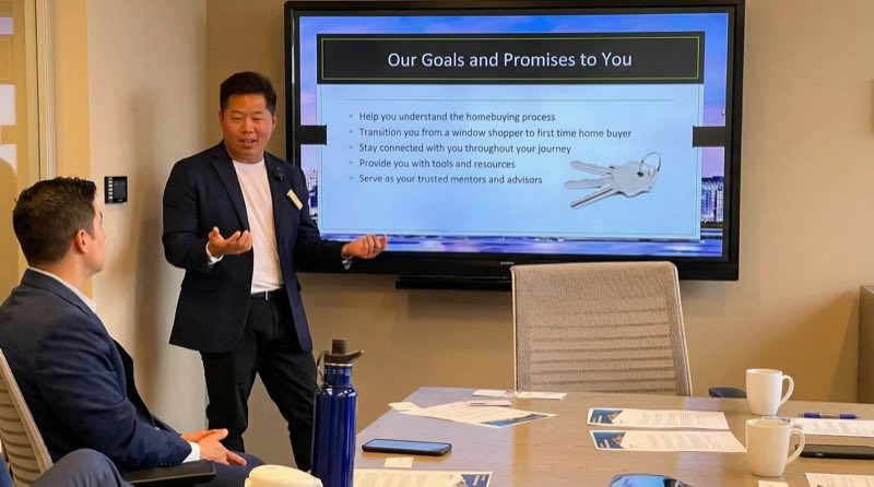 A mortgage advisor presenting a slide titled Our Goals and Promises to You in a conference room