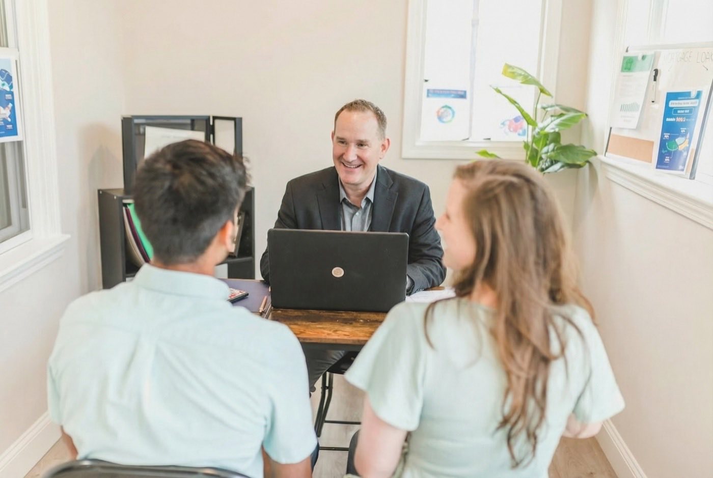 A loan officer smiling across a desk at a couple, an open laptop between them
