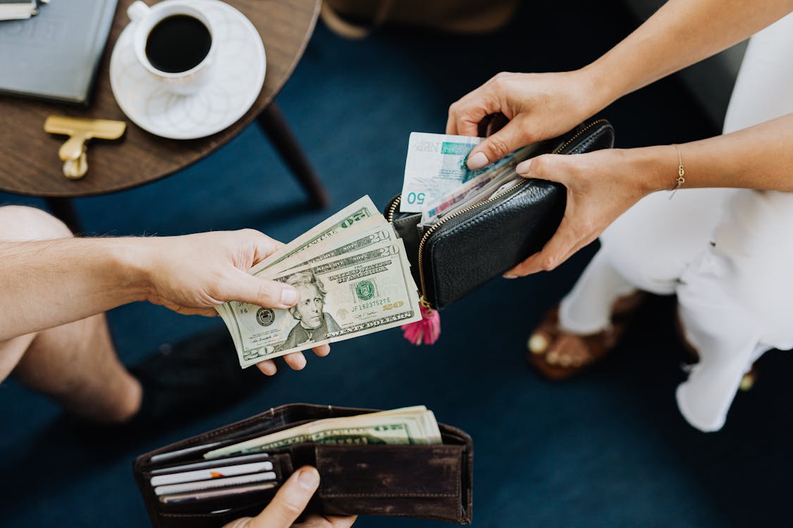 Two people counting cash from their wallets across a low table set with a cup of coffee