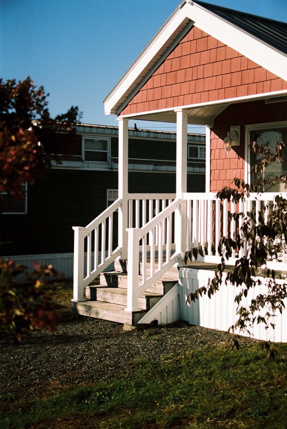 A small house with a covered porch and white railings, autumn leaves in the foreground