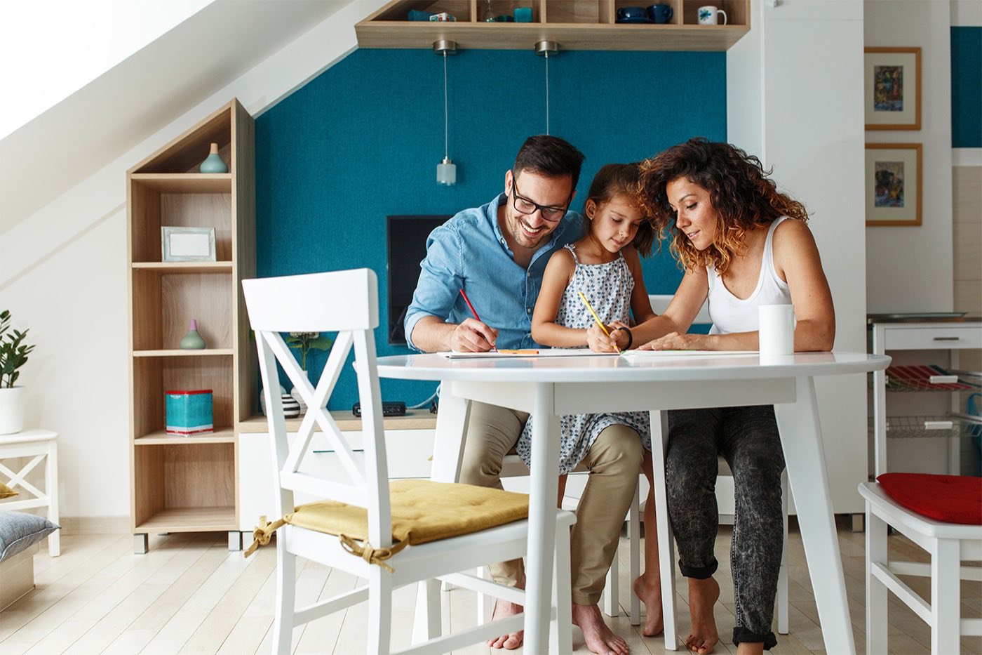 Two parents and a child drawing together at a white table in a bright kitchen