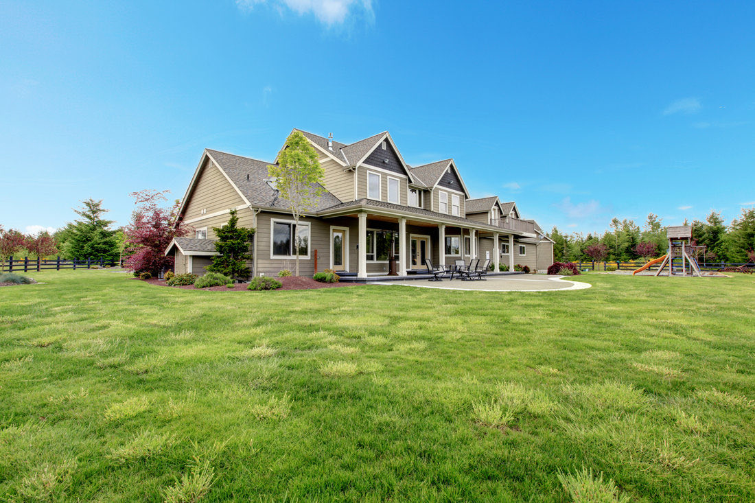 A large house at the far edge of a wide open lawn, with a play structure and open land beyond